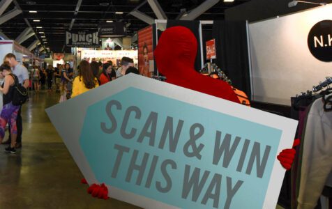 A sign waver holding a large arrow sign while wearing a bright red morph suit during an event